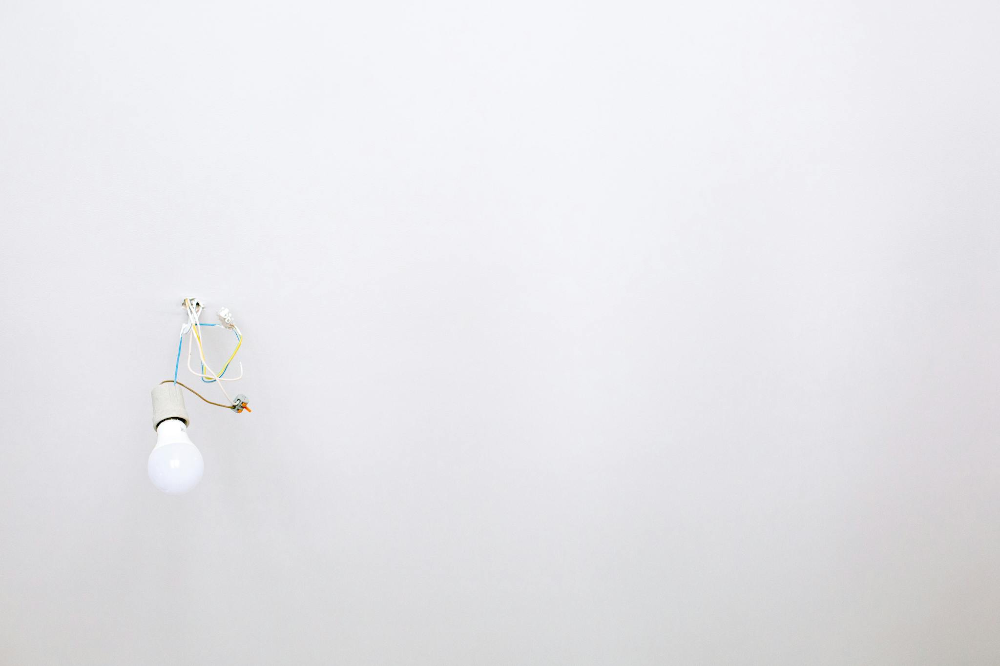 A minimalist light bulb with exposed wires hanging from a white ceiling, ideal for home renovation themes.