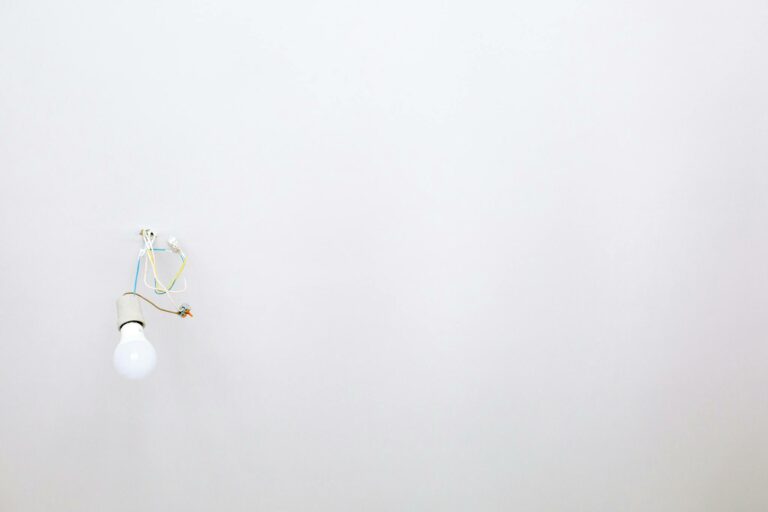 A minimalist light bulb with exposed wires hanging from a white ceiling, ideal for home renovation themes.